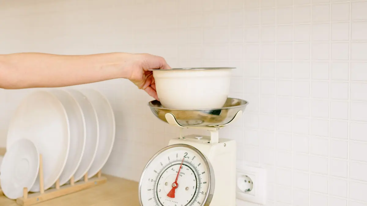 Una mano apoya un bol blanco sobre una balanza de cocina