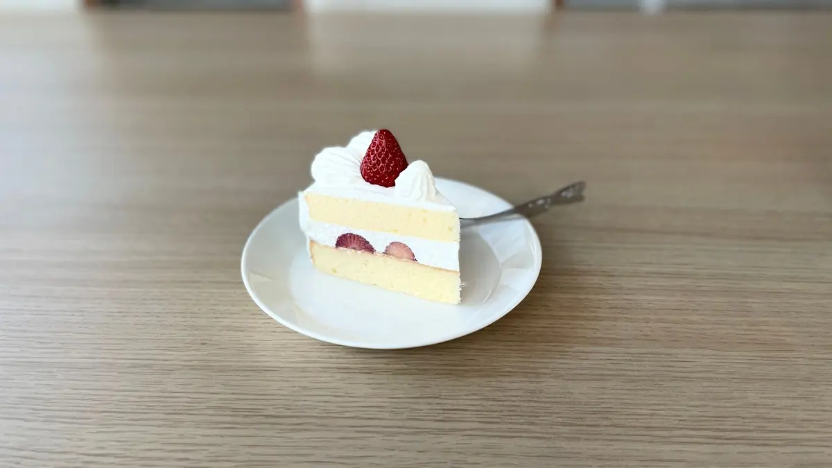 Una porción de torta con crema y una fresa encima, sobre un plato blanco y una mesa de madera