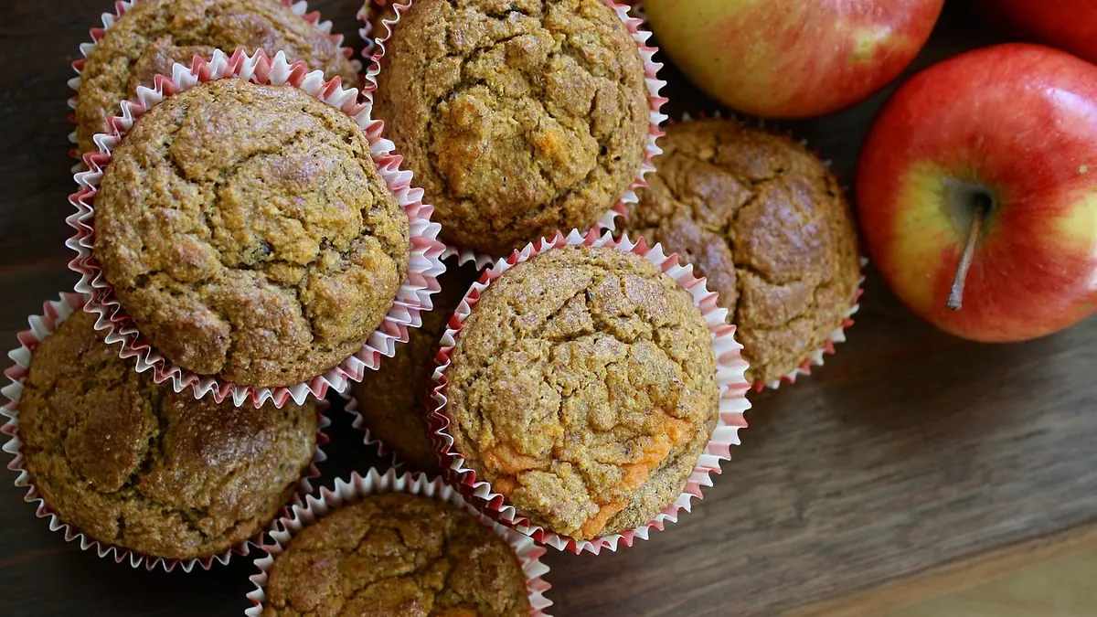 Muffins caseros dorados en moldes de papel, con unas manzanas rojas al lado, sobre una mesa de madera