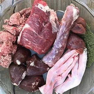Carne picada, un trozo de carne roja, corazones y cortes de ave crudos en una fuente de vidrio, preparados por una alumna del curso