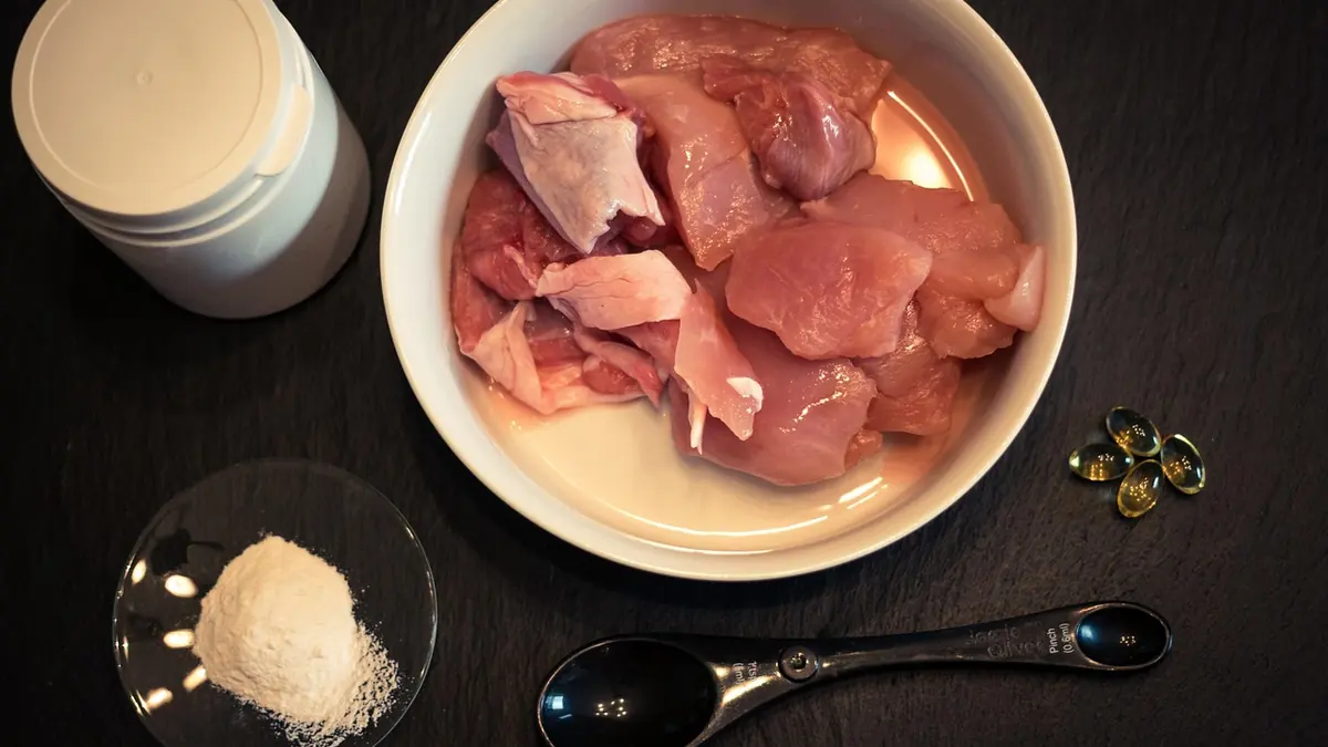 Un plato con carne cruda de pavo, un suplemento en polvo y cápsulas de aceite