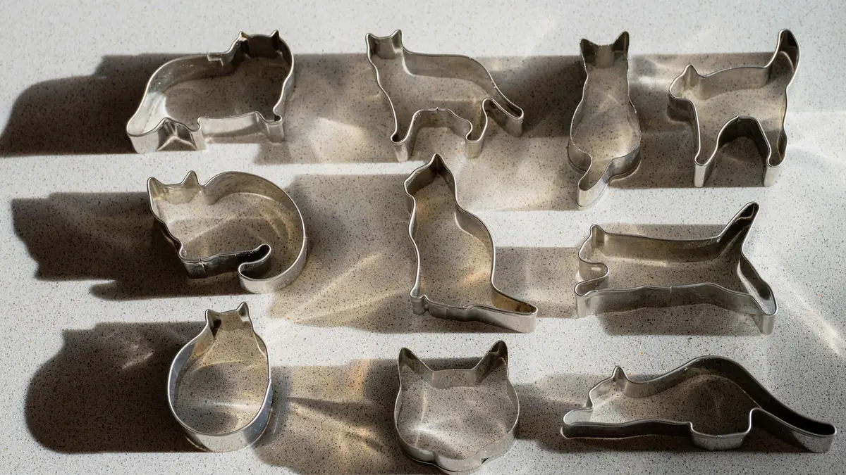 Cortadores de galletas de metal con forma de gato, en distintas posturas, sobre una superficie clara con sombras