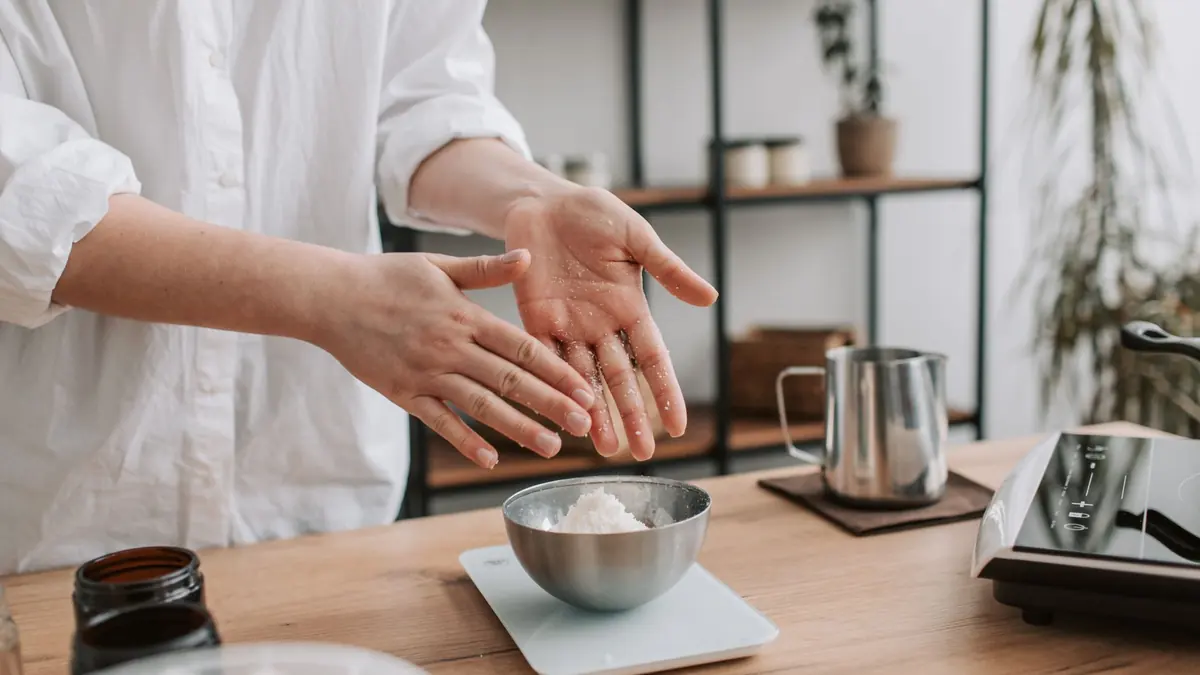 Un bol de acero con un polvo blanco sobre una balanza de cocina, con las manos abiertas de una persona al lado