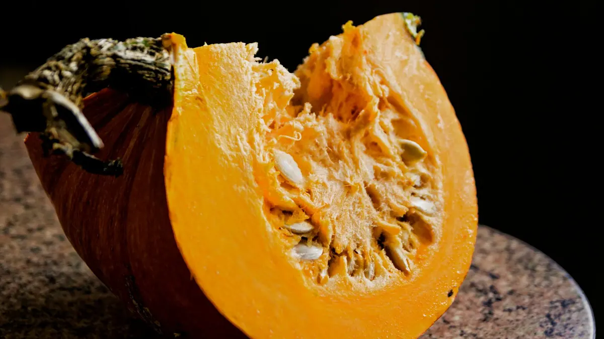 Un gajo de calabaza con su tallo seco y las semillas a la vista, sobre un fondo negro