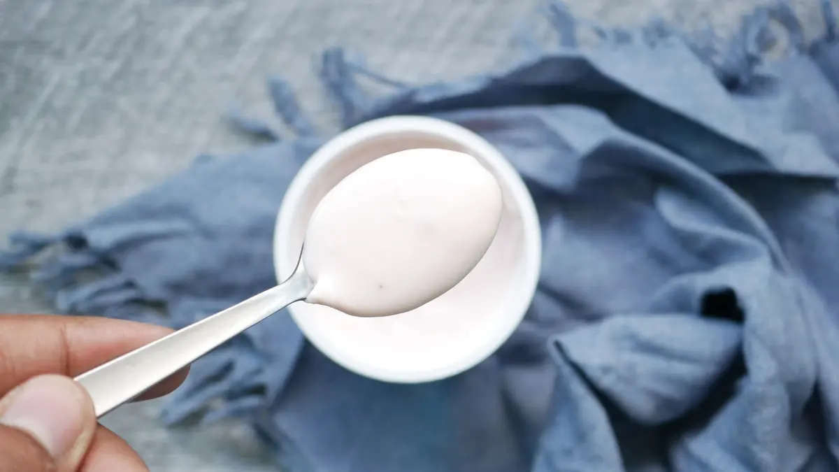 Una cuchara con yogur blanco sobre un cuenco, encima de una tela azul