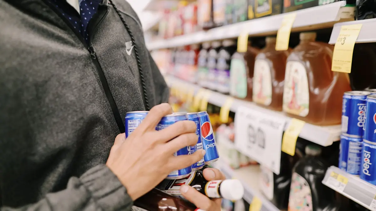 Una persona con latas de bebida en la mano frente a los estantes de un supermercado