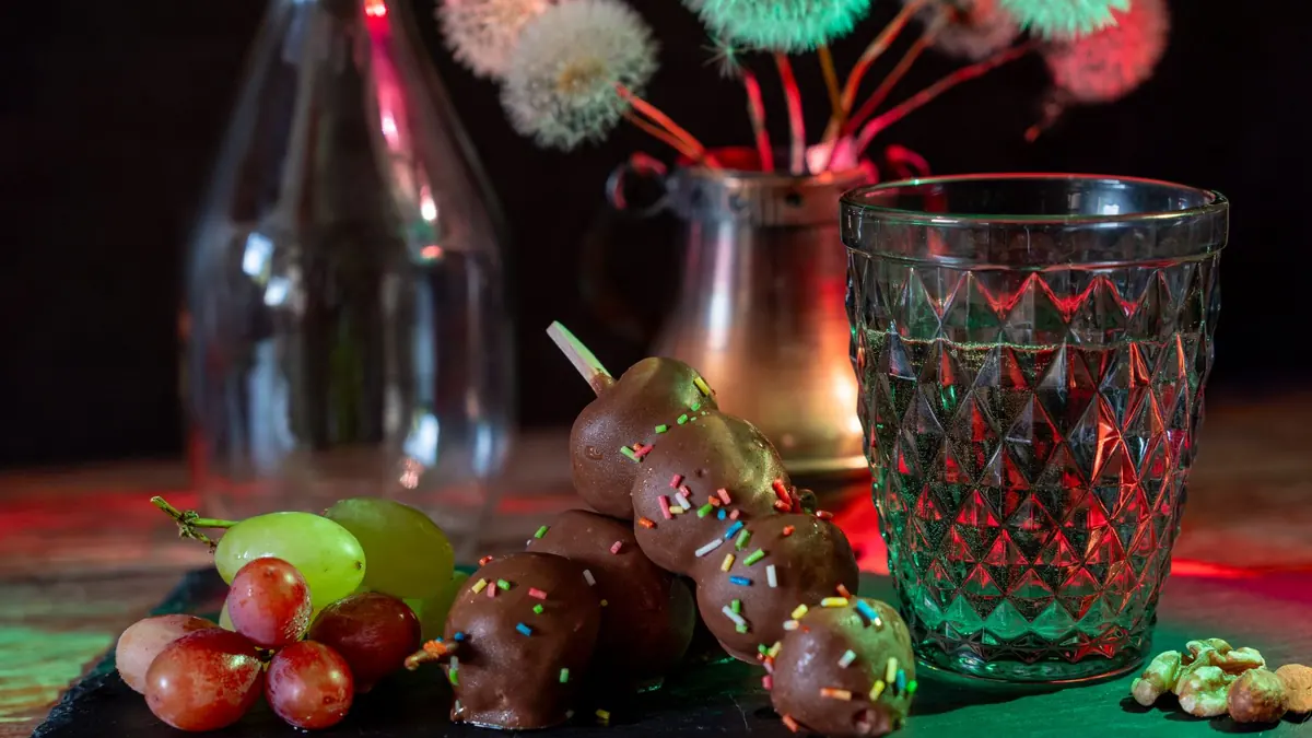 Bombones de chocolate con grageas de colores, uvas y nueces junto a un vaso de vidrio