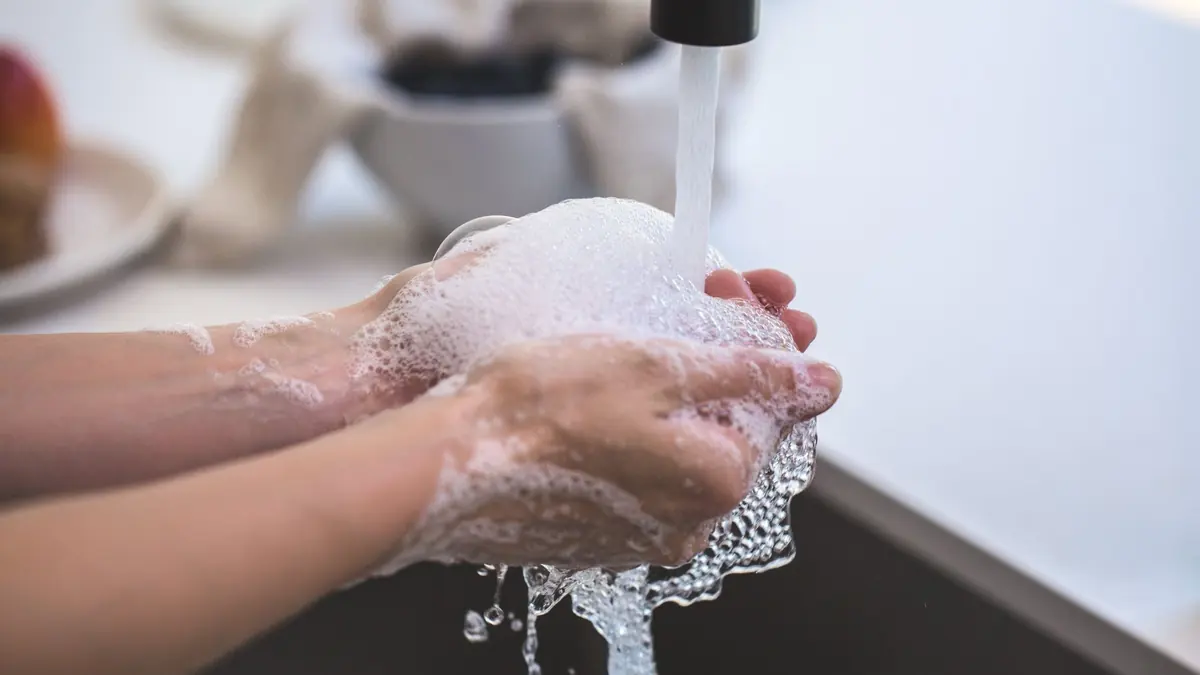 Dos manos con espuma de jabón bajo el chorro de agua de un grifo, con una cocina desenfocada atrás